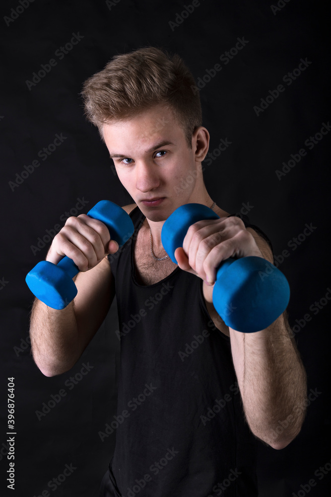 Young sportsman making exercises with dumbbels studio portrait on black background.