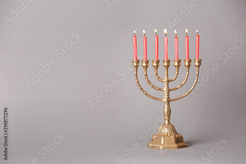 Golden menorah with burning candles on light grey background, space for text