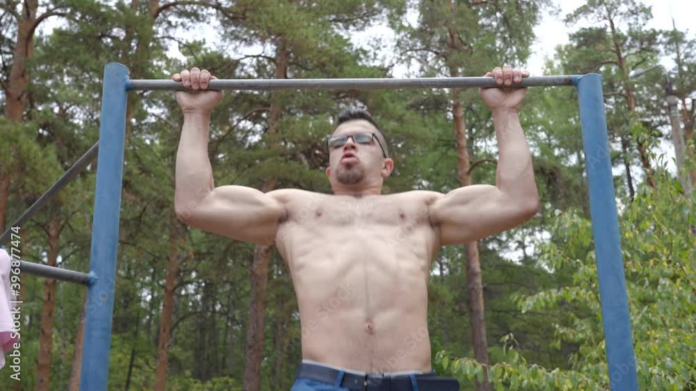 Guy bodybuilder of middle eastern appearance pulls himself up on a horizontal bar in the forest. Guy bodybuilder of middle eastern appearance pulls himself up on a horizontal bar in the forest.