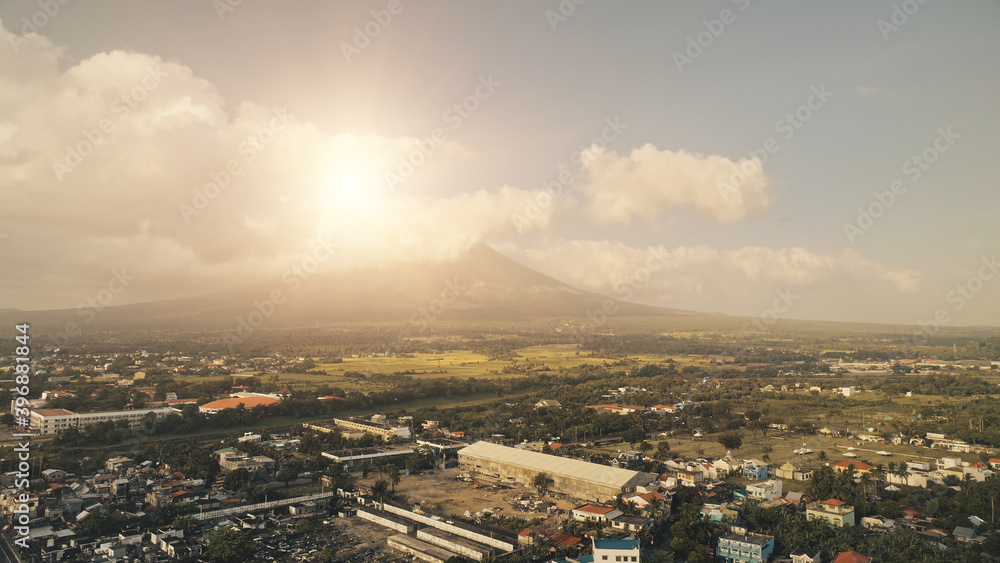 Sun shine over Mayon volcano erupt at Legazpi cityscape aerial. Epic Philippines landmark at urban buildings and roads. Green grass valley of mount hillside. Cinematic nature and tropic town