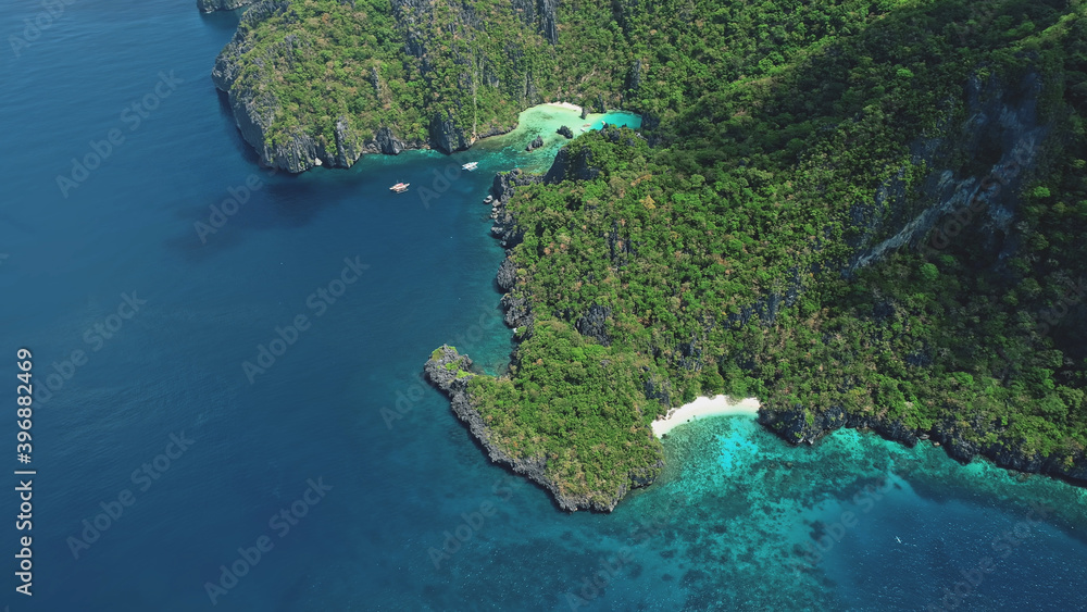 Top down green mountainous island at ocean bay in aerial view. Small passenger boats at coast sea water. Tropical nature landscape with white sand beach of Palawan Island, Philippines, Asia