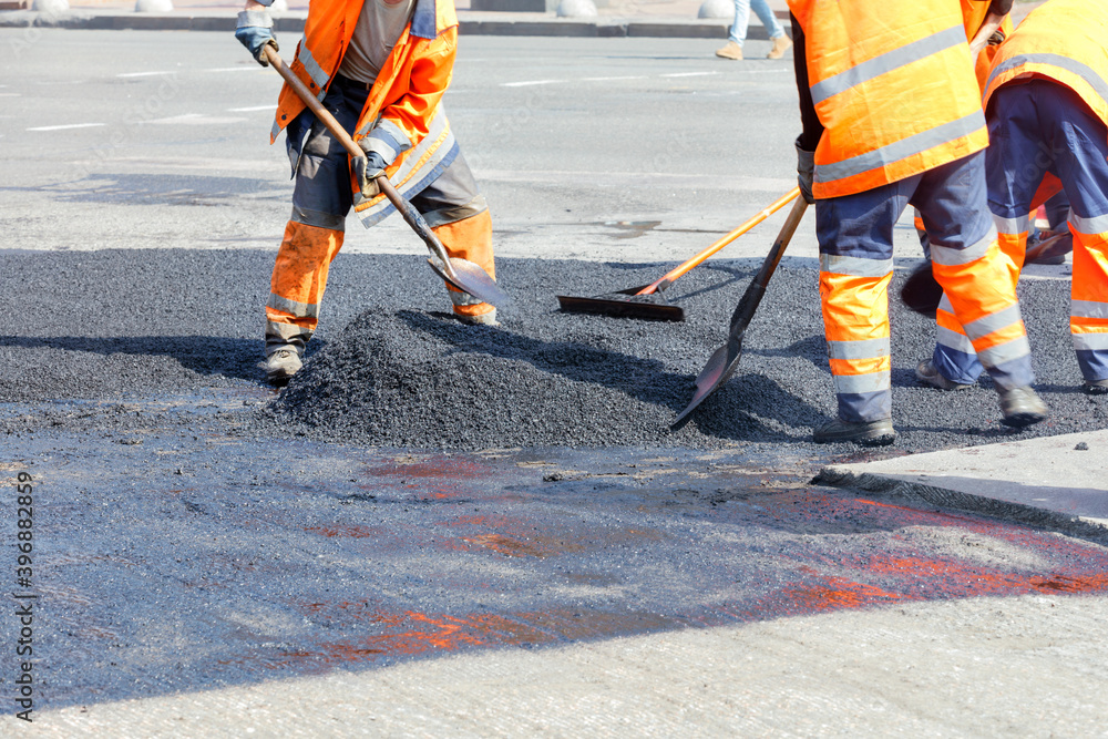 Partial road repair, the working team manually levels the hot asphalt with shovels and metal strips.