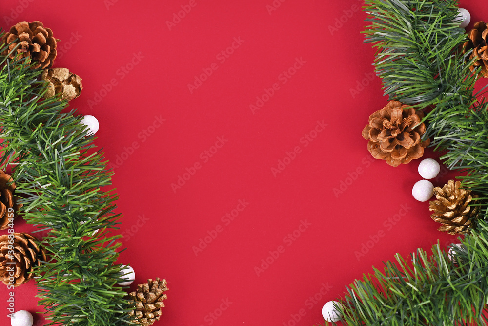 Christmas background with seasonal fir garlands, fir cones and white snowball ornaments with empty red copy space in middle