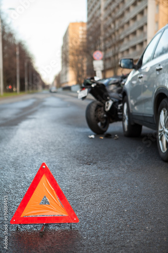 Triangular safety reflector is on asphalt road, sign is on the distance of car and motorcycle crash