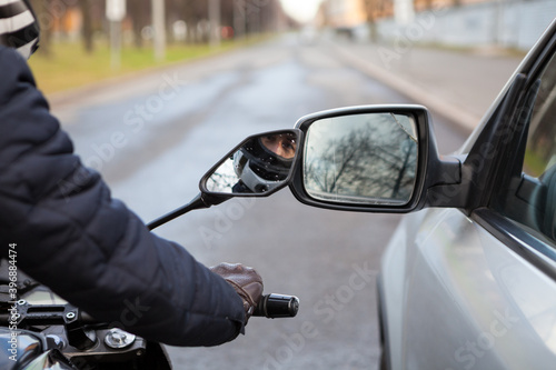 Motorcycle rider touching side mirror of a car when riding nearby on a road, close up view