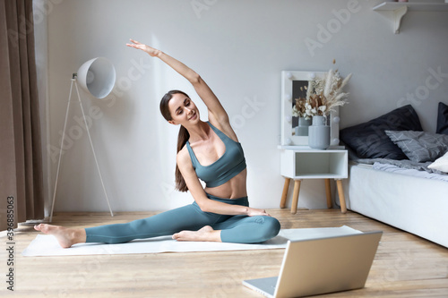 Young sporty fit slim woman coach do practice video online training yoga laptop in living room at home