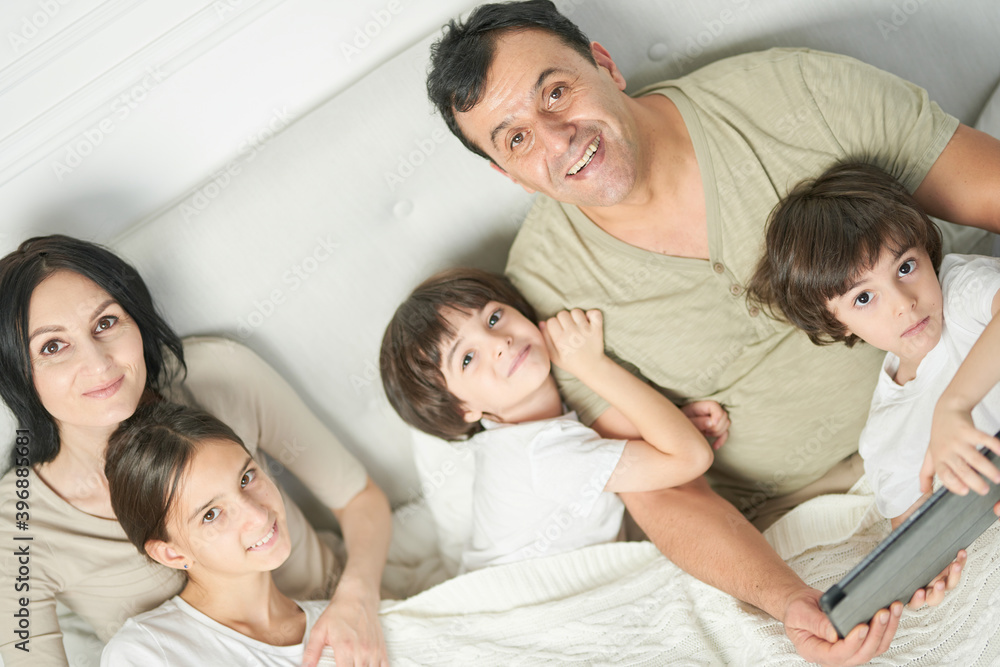 Together at home. Portrait of happy latin famile, little kids and parents smiling at camera while spending time together, staying in bed in the morning Together at home. Portrait of happy latin famile, little kids and parents smiling at camera while spending time together, staying in bed in the morning