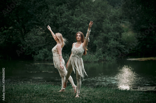 Two beautiful young women dancing in nature. There is a large lake behind. The concept of natural cosmetics and harmony with nature. My hair is blowing in the wind.