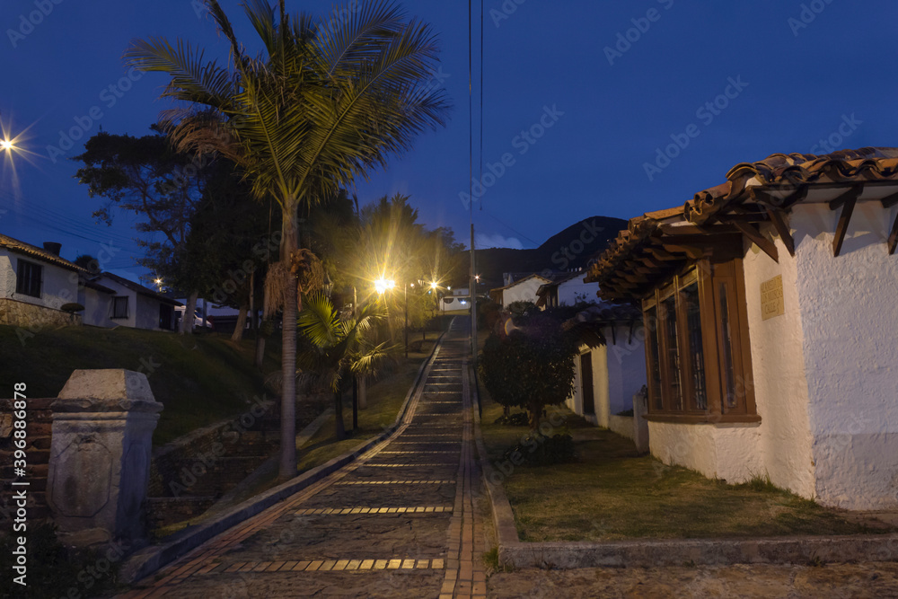 GUATAVITA, COLOMBIA - Colombian guatavita colonial town night scene of an empty brick peatonal path near to a grass canal and a white house. 