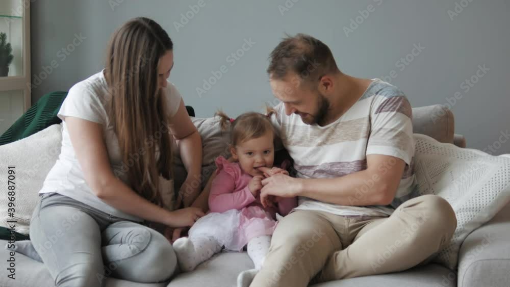 Parenthood. Young parents playing with their cute little daughter on sofa. Young carefree parents and child laugh play cuddling at home enjoy funny game on couch. Young family of three. Mum and dad Parenthood. Young parents playing with their cute little daughter on sofa. Young carefree parents and child laugh play cuddling at home enjoy funny game on couch. Young family of three. Mum and dad