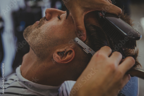 detail of a young man with tattooed arms cuts a man's hair in a barber shop