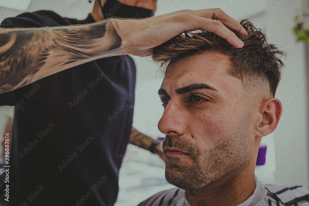 Fototapeta premium a young man with tattooed arms cuts a man's hair in a barbershop