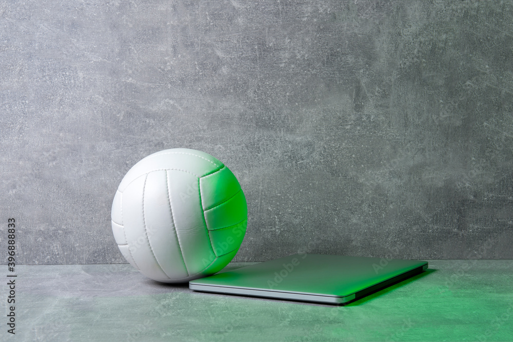 White Volleyball ball and grey laptop on grey background. Online workout concept White Volleyball ball and grey laptop on grey background. Online workout concept