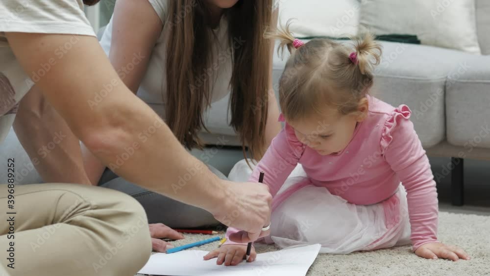 Cute small kid girl artist playing with parents drawing coloring picture on floor, focused smart preschool child enjoying creative art hobby activity at home, children development concept Cute small kid girl artist playing with parents drawing coloring picture on floor, focused smart preschool child enjoying creative art hobby activity at home, children development concept