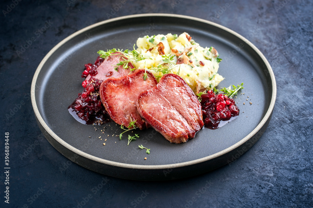 Traditional fried cured and sliced veal tongue with mashed potatoes and cranberries relish offered as close-up in a Nordic design plate