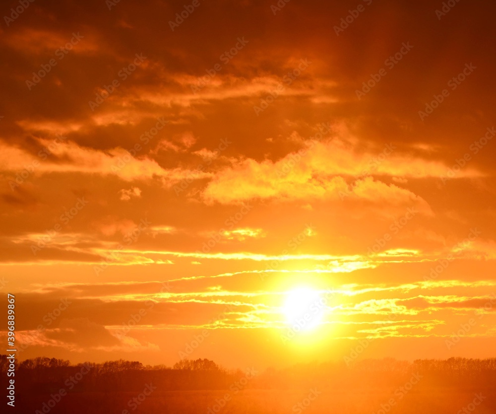 Fototapeta premium Сфотографирован закат с оранжевыми облаками и ярким белым солнцем