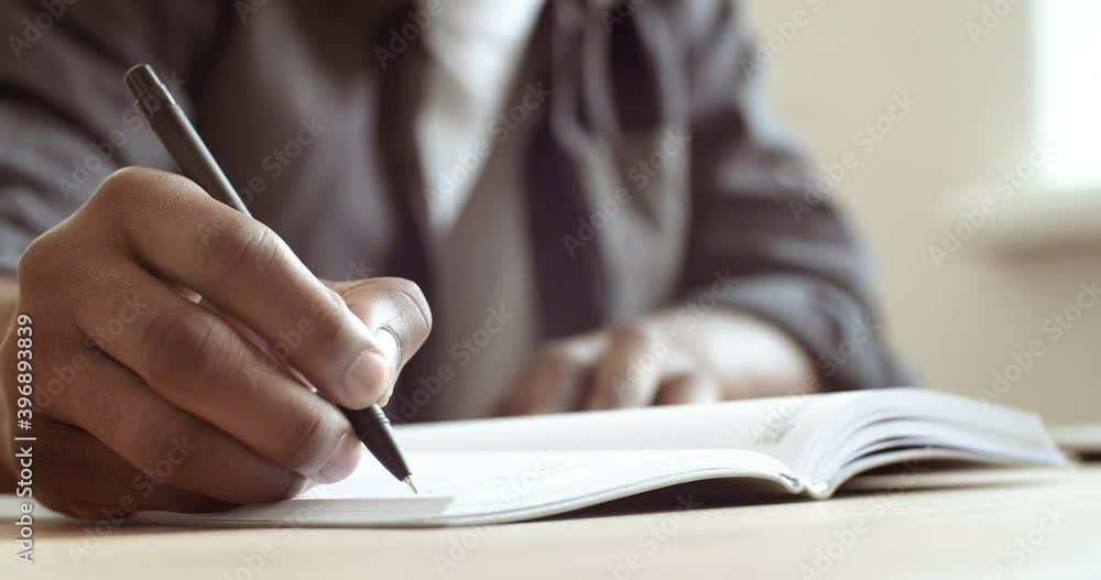 Close-up male hand holds pen makes notes on sheet of paper signs document. Cropped frame african american man writing with pencil report outline outline working studying from home sitting at table