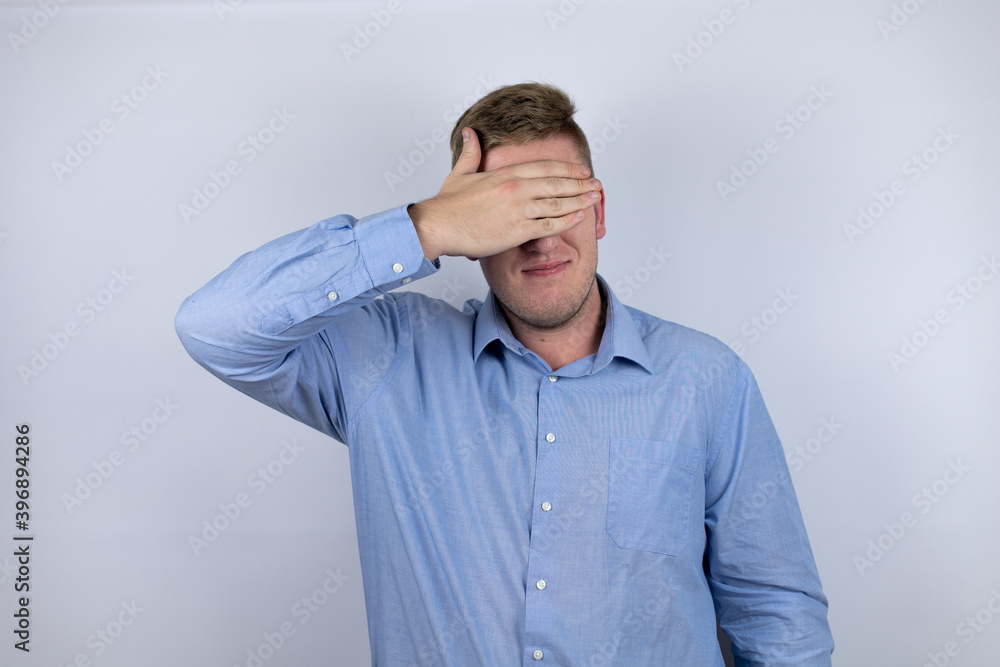 Business young man wearing a casual shirt over white background serious and covering her eyes with her hand Business young man wearing a casual shirt over white background serious and covering her eyes with her hand