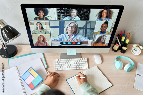 Online remote high school class concept. Mixed race college student distance learning at home on desk using computer conferencing with teacher and classmates group virtual meeting on screen. Top view