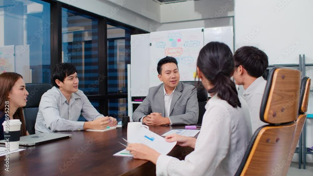 Group of happy Asian business people discuss together in team brainstorm meeting and clap hand, work late night in office. Corporate business, coworker teamwork, or project success celebration concept Group of happy Asian business people discuss together in team brainstorm meeting and clap hand, work late night in office. Corporate business, coworker teamwork, or project success celebration concept