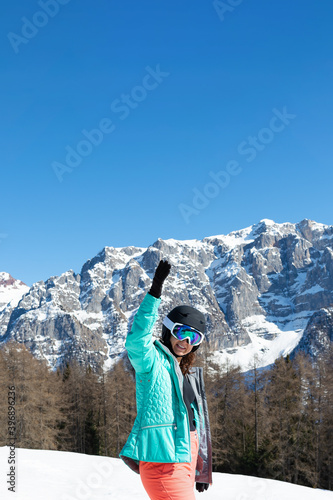 A woman in a colorful ski suit, helmet and sunglasses after skiing stands against the backdrop of mountain peaks. Sports concept, people, travel.