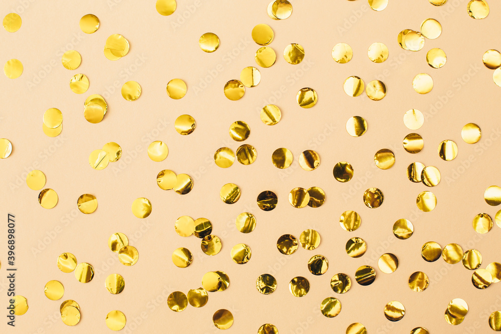 Gold confetti on beige paper background. Festive holiday backdrop. Birthday congratulations Christmas New Year. Flat lay, top view, copy space. Gold confetti on beige paper background. Festive holiday backdrop. Birthday congratulations Christmas New Year. Flat lay, top view, copy space.