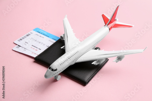 Toy airplane and passport with tickets on pink background