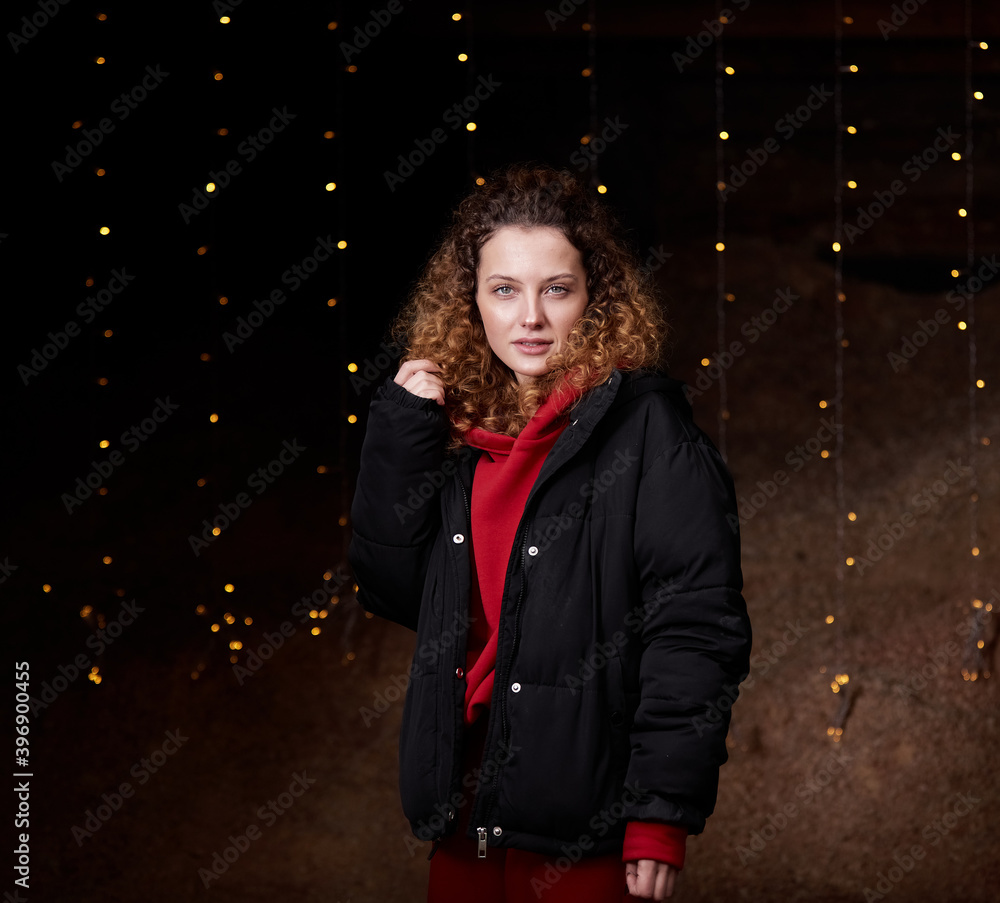 A beautiful curly-haired girl stands on a black background in the New Year's lights A beautiful curly-haired girl stands on a black background in the New Year's lights