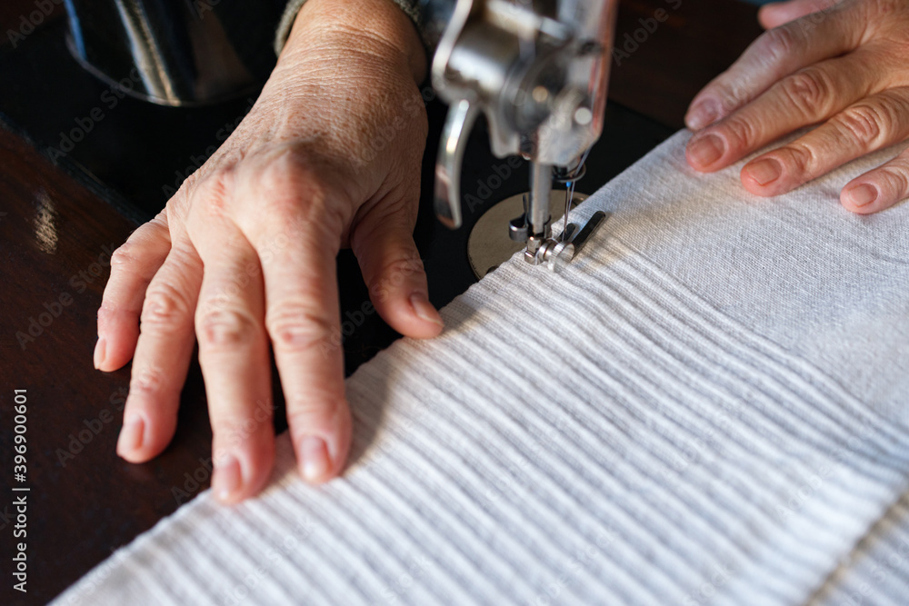 Obraz premium Old woman hands using an old sewing machine