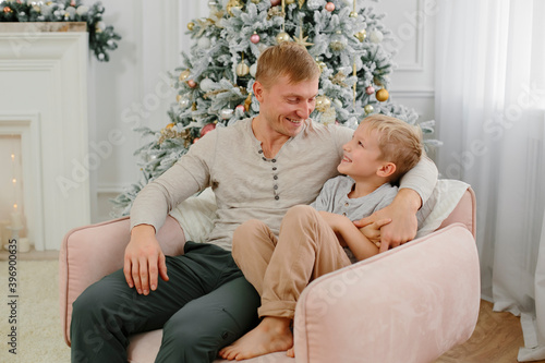 father and son are sitting in a large pink armchair against the background of a Christmas tree. European family. christmas and new year concept