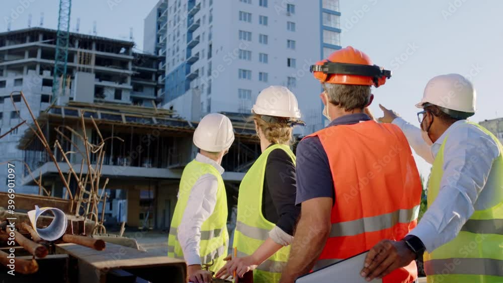 Concept of Covid-2019 group of engineers and architects working together at construction site they wearing protective mask analyzing the plan of construction they wearing safety helmets and goggles Concept of Covid-2019 group of engineers and architects working together at construction site they wearing protective mask analyzing the plan of construction they wearing safety helmets and goggles