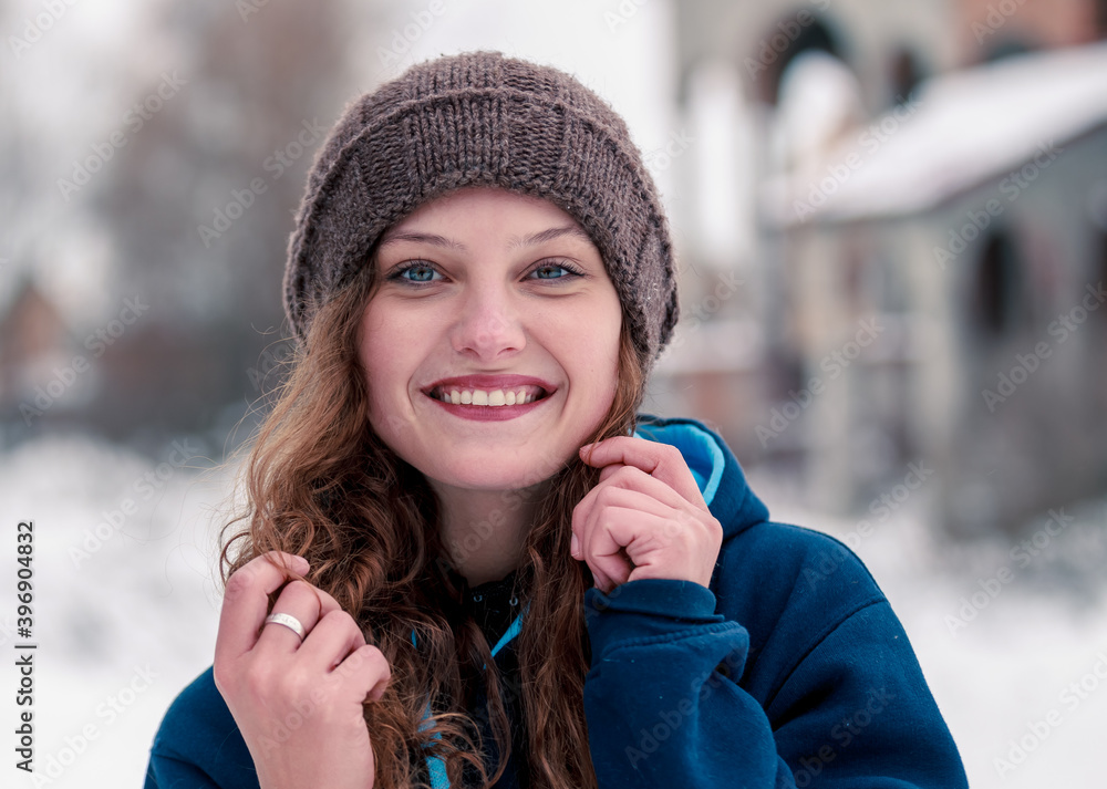 Portrait of a beautiful curly girl with a smile in a winter hat on a background of snow Portrait of a beautiful curly girl with a smile in a winter hat on a background of snow