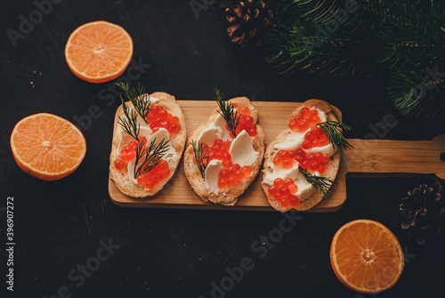 Sandwiches with red caviar and red fish on wooden planks black background.