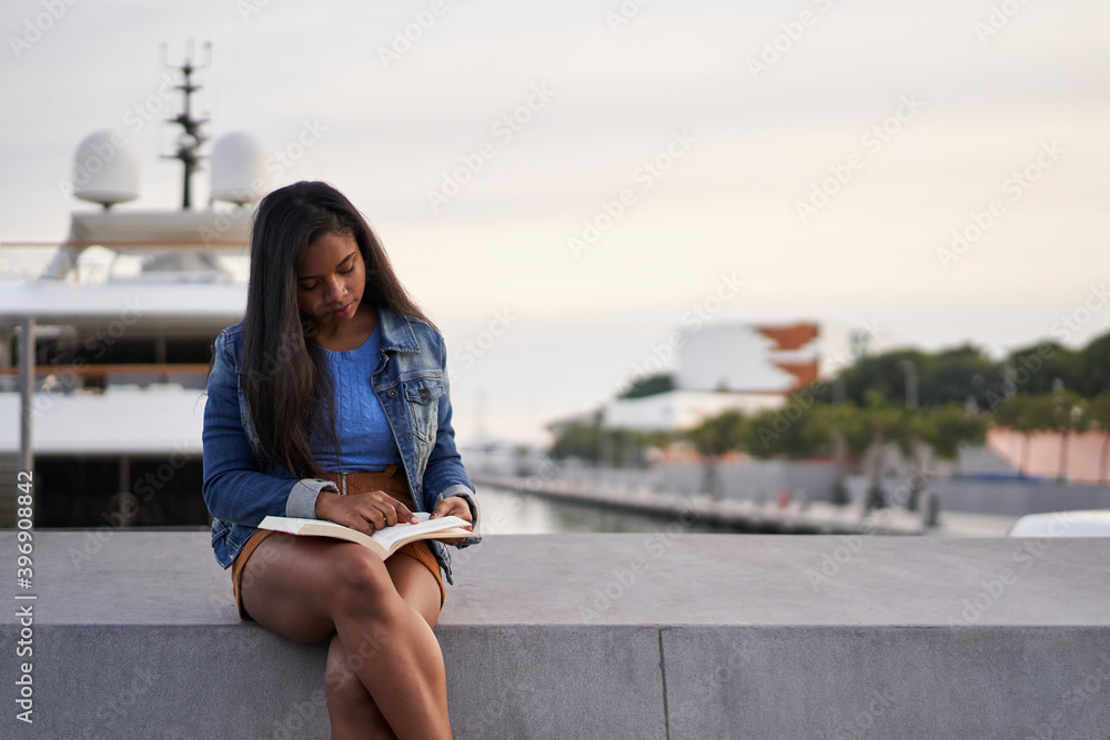 Portrait of an African American black woman reading a book sitting on a ...