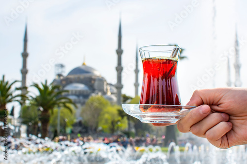 Photography Woman's hand holding cup with Traditional turkish tea in front of Blue mosque (aka Sultanahmet Camii) in Istanbul, Turkey