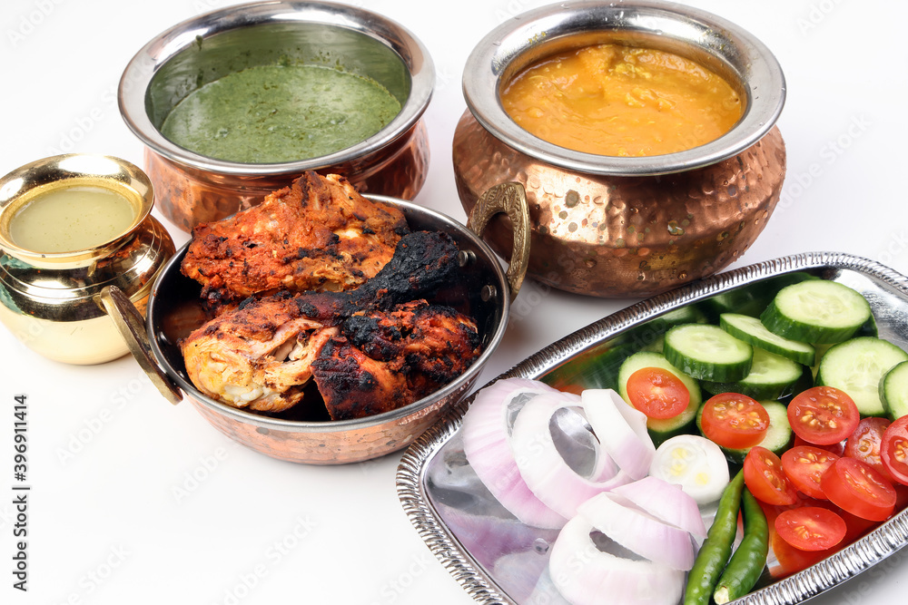 Spicy red Chicken grilled tikka tandoori nan bread green spinach curry yogurt sauce dal tomato cucumber onion salad set in metal stainless steel brass copper pot on white background