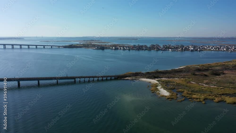 An aerial shot of elevated train tracks with s swing bridge over a bay in Queens, NY. The camera trucks left & pan right over the water. The sun is shining on the water & it is a beautiful day. An aerial shot of elevated train tracks with s swing bridge over a bay in Queens, NY. The camera trucks left & pan right over the water. The sun is shining on the water & it is a beautiful day.