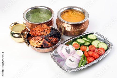 Spicy red Chicken grilled tikka tandoori nan bread green spinach curry yogurt sauce dal tomato cucumber onion salad set in metal stainless steel brass copper pot on white background