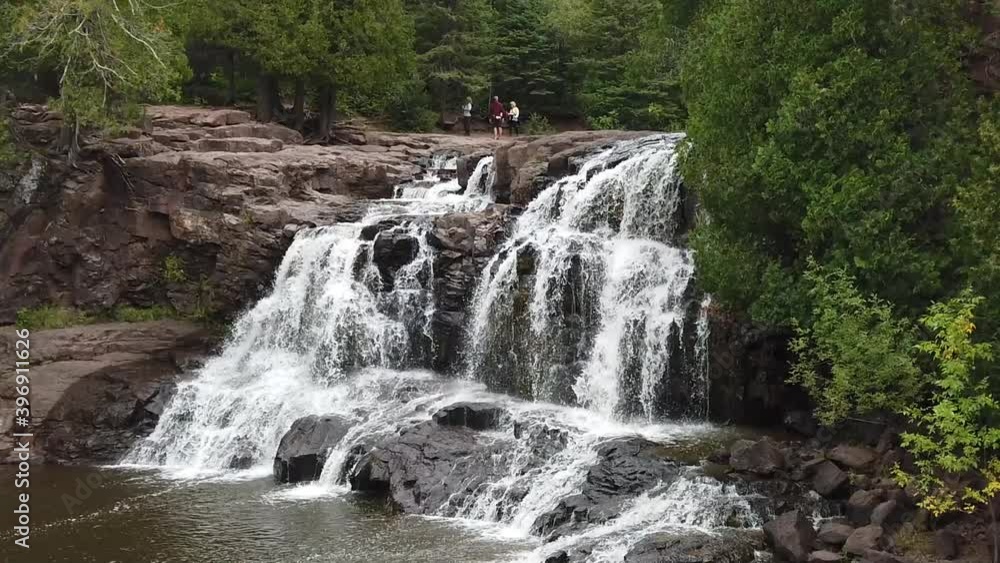 Slow motion view of large rushing waterfall on summer day near Duluth, MN. Waterfall surrounded by lush, green trees and vegetation. Daytime, outdoors, bright light. Slow motion view of large rushing waterfall on summer day near Duluth, MN. Waterfall surrounded by lush, green trees and vegetation. Daytime, outdoors, bright light.