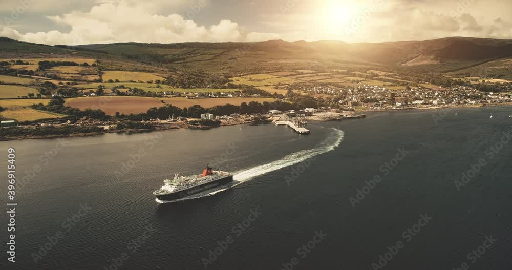 Ferry terminal of sun pier town at ocean gulf aerial. Ship sail at green land, mountains. Nobody nature seascape. Water transportation. Cinematic drone shot. Brodick, Arran Island, Scotland, Europe Ferry terminal of sun pier town at ocean gulf aerial. Ship sail at green land, mountains. Nobody nature seascape. Water transportation. Cinematic drone shot. Brodick, Arran Island, Scotland, Europe