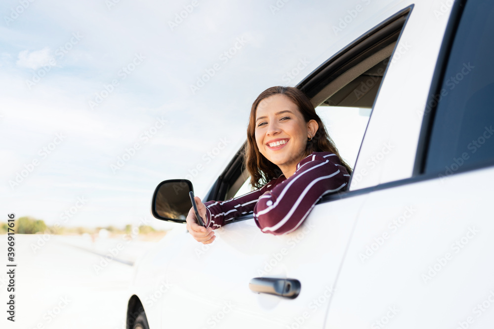 Naklejka premium Happy woman looking out her window car with her cellphone