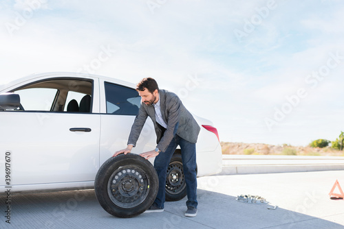Hispanic man moving a spare tire next to his car © AntonioDiaz