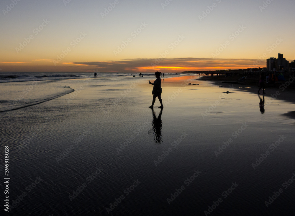 Silhouettes in the sunset at the beach: woman walking on the wet sand to take a snap Silhouettes in the sunset at the beach: woman walking on the wet sand to take a snap