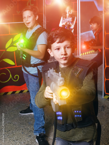 active young boy aiming laser gun at other players during lasertag game in dark room