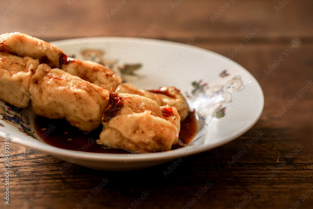 Closeup and crop snack vegan food (fried tofu) in white ceramic plate on wooden background. Thai and Chinese people popular eaten vegan foods in Chinese vegetarian festival in October every years. Closeup and crop snack vegan food (fried tofu) in white ceramic plate on wooden background. Thai and Chinese people popular eaten vegan foods in Chinese vegetarian festival in October every years.