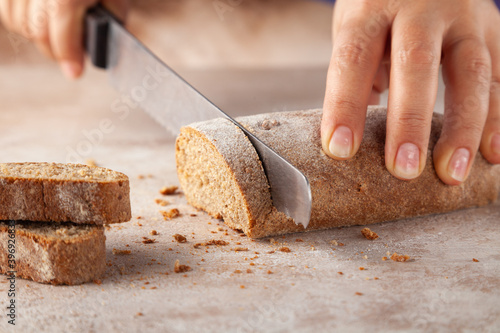Close-up baker hands, chopping cereal bread with knife