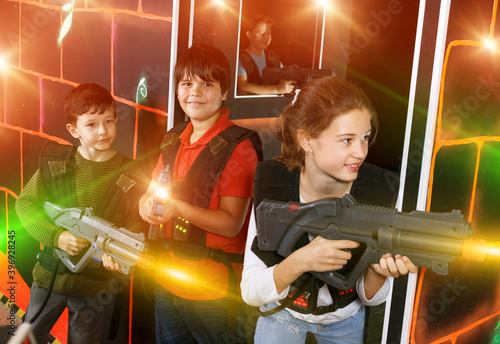 Cheerful teenage girl and boys with laser guns playing laser tag on dark room