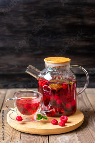 Herbal tea with berries, raspberries, mint leaves and hibiscus flowers in glass teapot and cup on wooden table Medicine for cold Vitamin drink Rustic style