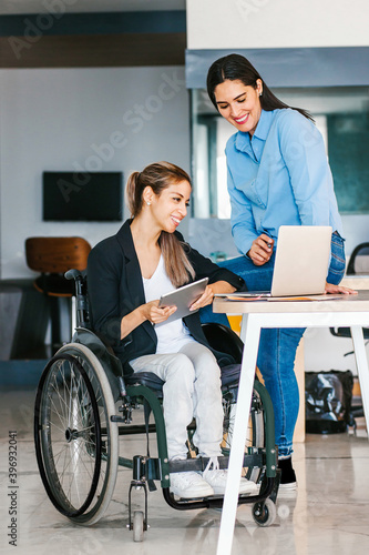 Latin woman in wheelchair working with computer in office in Mexico city with her colleague
