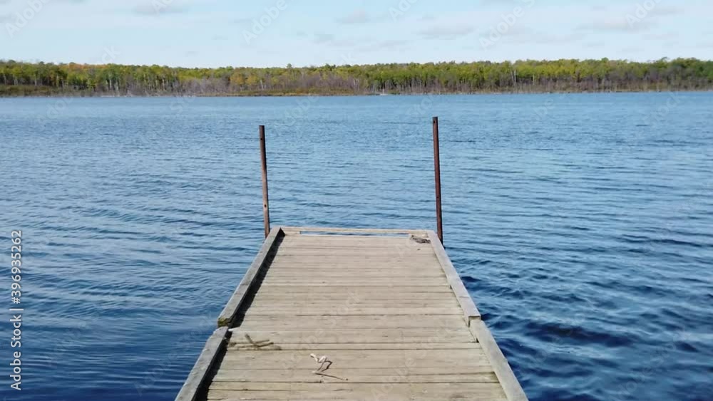 Slow motion moving along old wooden dock on clear blue lake with cloudy sky and green trees in the distance. Outside, bright, summertime. Slow motion moving along old wooden dock on clear blue lake with cloudy sky and green trees in the distance. Outside, bright, summertime.